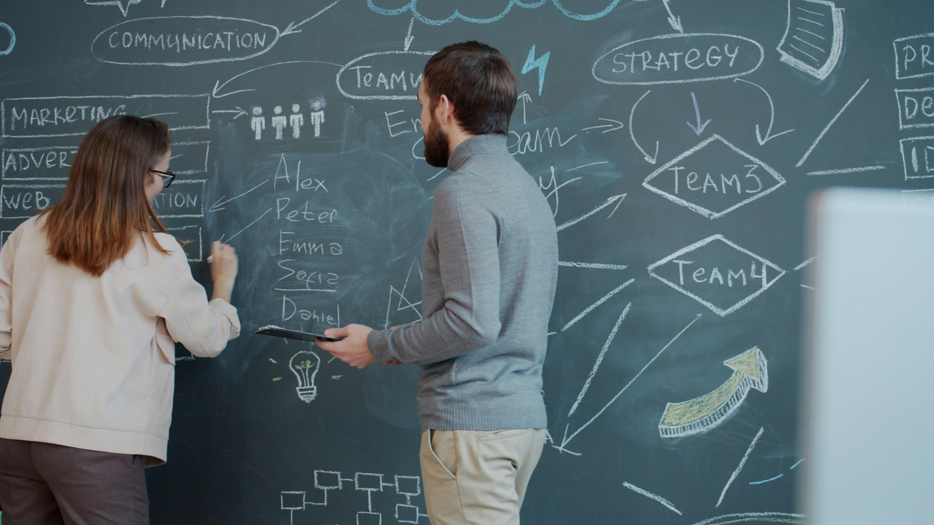 Two people planning a strategy with diagrams on a chalkboard